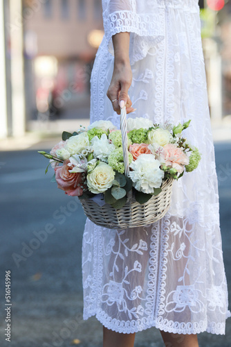 a basket of flowers in the hands of a girl in a white lace dress