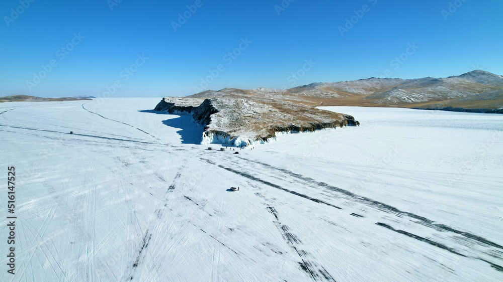 Fototapeta premium Frozen Lake Baikal from the air. Roads on the ice of the lake. Winter travel by car.