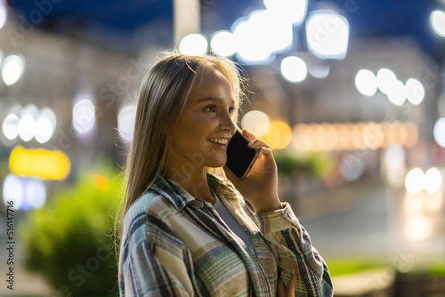 Beautiful young woman talking on mobile phone, walking in night city