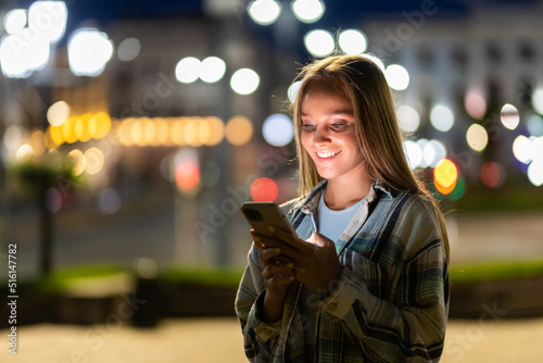 Young woman texting cell phone in city at night