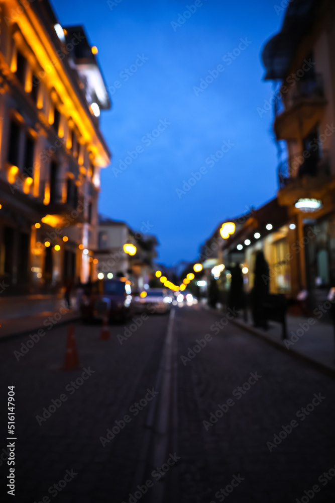 Blurred view of beautiful cityscape with glowing streetlights and illuminated building in evening