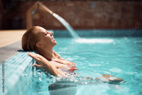 Smiling woman with eyes closed relaxing in water at swimming pool on summer day.
