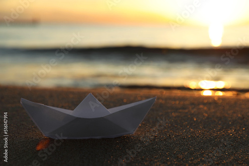 White paper boat on sand near sea at sunset  closeup. Space for text