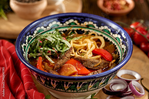 Eastern food - soup shourpa with vegetables and lamb meat on wooden table. Traditional uzbek soup with lamb meat, sweet pepper, tomatoes in rustic style. Caucasian cuisine on dark wooden background.