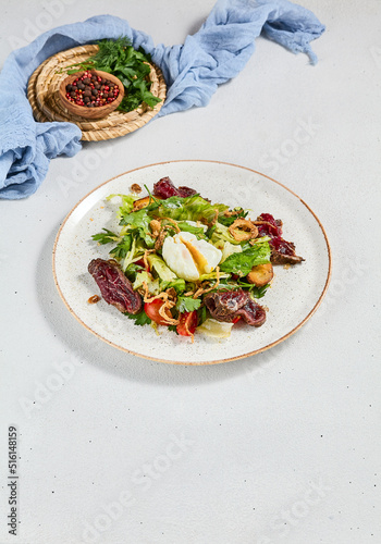 Green salad with sliced roast beef and pachot egg. Roast beef salad with vegetables and egg on concrete background in minimal style. Aesthetic composition with meat salad, textile and spices.