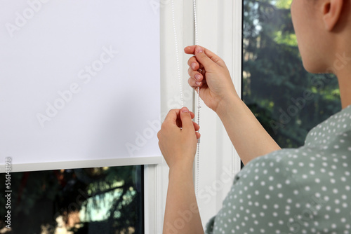 Fotografie Woman opening white roller blind on window indoors, closeup
