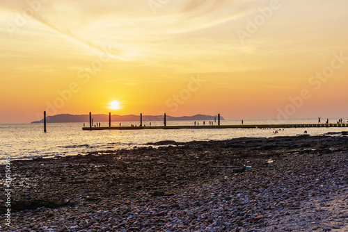 Landscape of colorful sunset shining over bright orange waters of the ocean. Silhouette of tourists walking  relaxing and taking photos sundown on beach of tropical sunset at Koh Larn Beach.