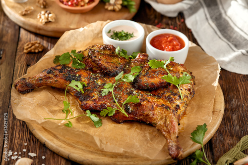 Traditional georgian dish - chicken tabaka on wooden background in rustic style. Roasted whole chicken in georgian style on wooden table. Chicken tabaka with sauces in rustic style.