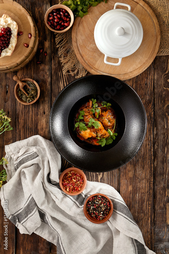 Traditional georgian food - chicken chakhokhbili in black plate on wooden background. Georgian chicken stew with herbs on wooden table. Chakhokhbili with tomatoes and herbs in rustic style.