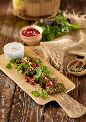 Traditional georgian food - meat dolma on plate with sauce in rustic style. Caucasian dish - stuffed grape leaves with minced meat and pomegranate on wooden background. Composition with meat dolma.