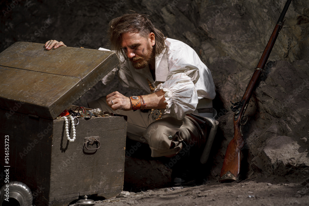 Sea robber captain of pirate ship armed with treasure chest in cave. Concept historical halloween. Filibuster cosplay Sea robber captain of pirate ship armed with treasure chest in cave. Concept historical halloween. Filibuster cosplay