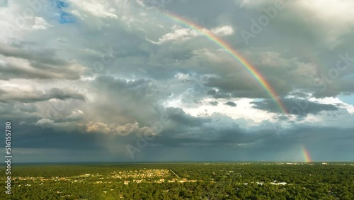 Colorful rainbow against landscape of dark ominous clouds forming on stormy sky before heavy thunderstorm over rural town area photo