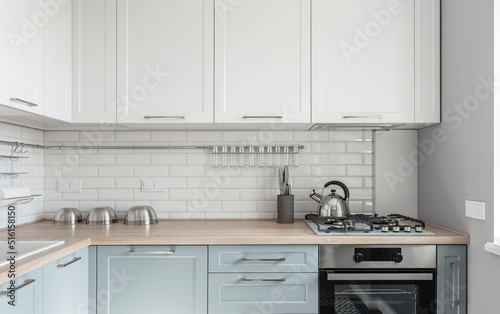 Design of a modern small light white kitchen with a blue kitchen cabinets and loft lamps. High quality photo