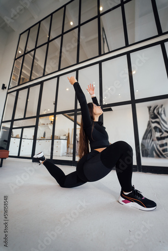 Young female wearing black sports suit exercising yoga pose indoors.