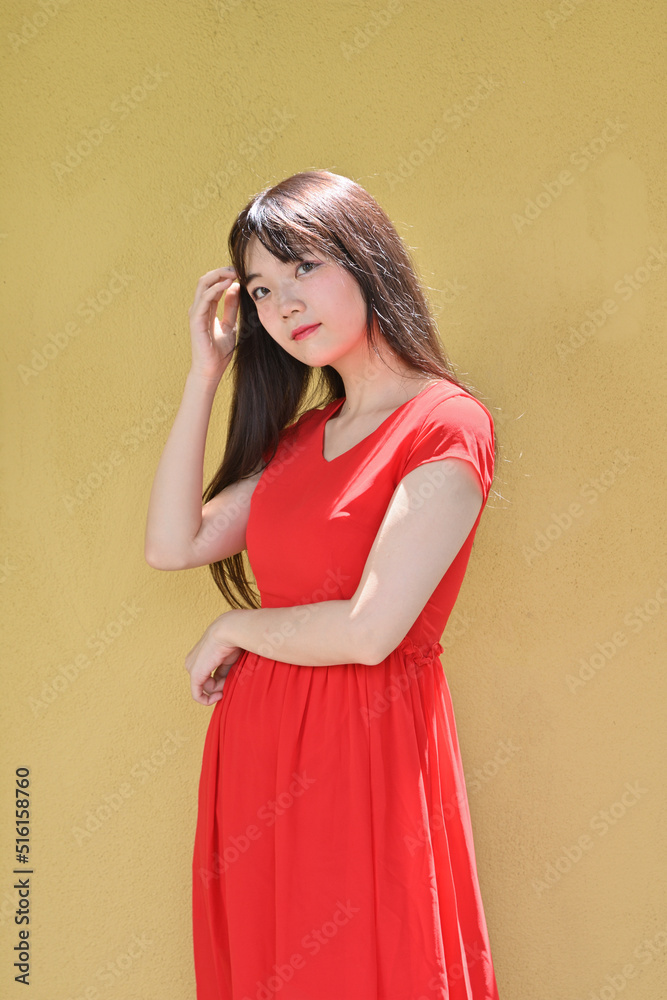 Fototapeta premium 黄色い壁に佇む赤いワンピースの女性