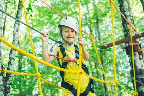Little girl overcomes the obstacle in the rope park. Child enjoying activity in a climbing adventure park on a summer day. 