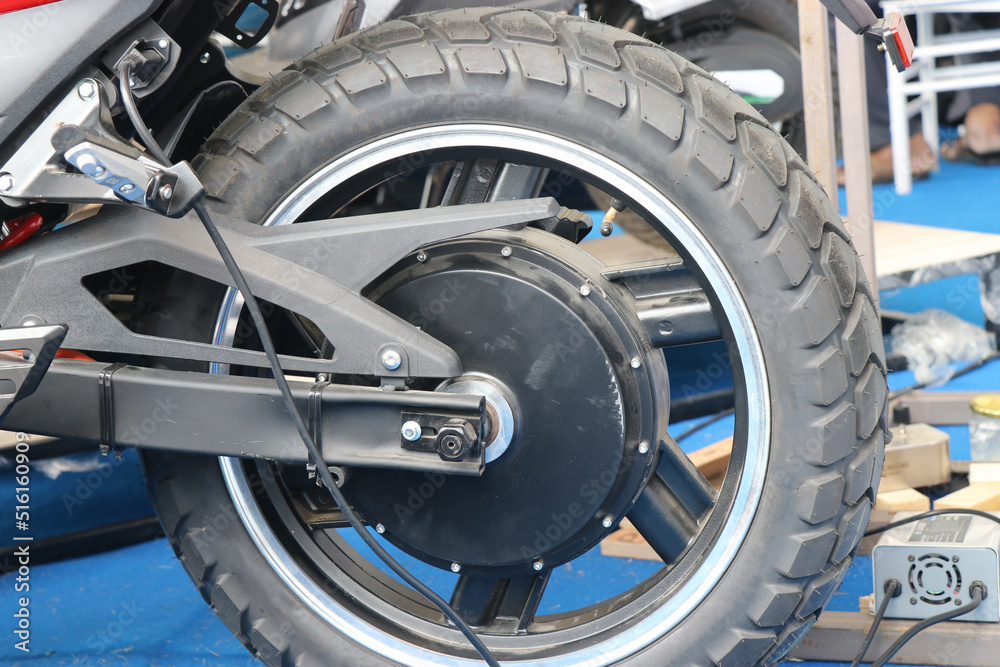 Sport electric motorcycle rear wheel view. Back side wheels with brushless motor view and bike connected to charging Sport electric motorcycle rear wheel view. Back side wheels with brushless motor view and bike connected to charging
