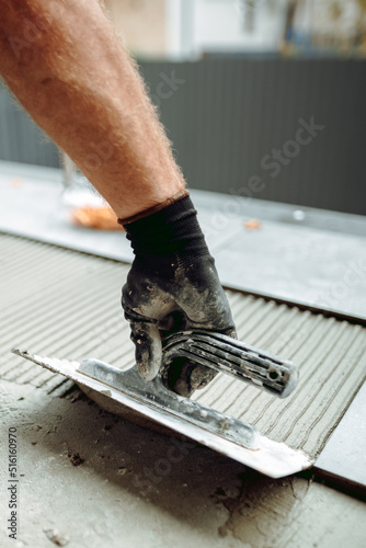 Flooring and tiling. Hand of professional construction worker placing floor tiles on adhesive surface on balcony