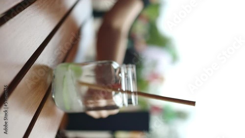 Cold summer mojito cocktail in a glass. Woman hand takes a glass of tropical drink mojito with eco straws photo