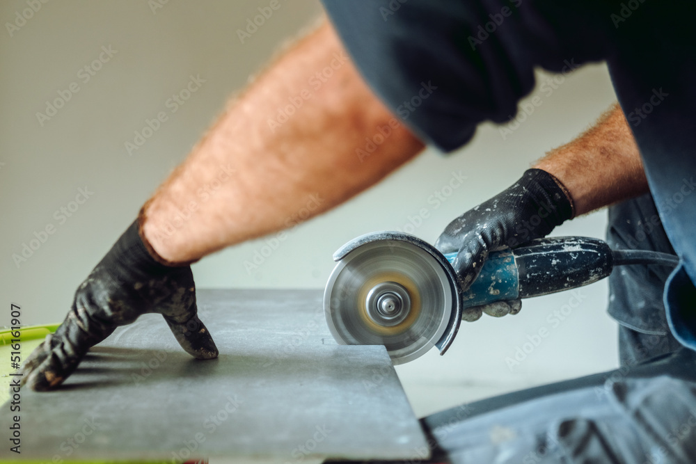 professional caucasian construction worker cutting ceramic tiles with angle grinder during tiling works