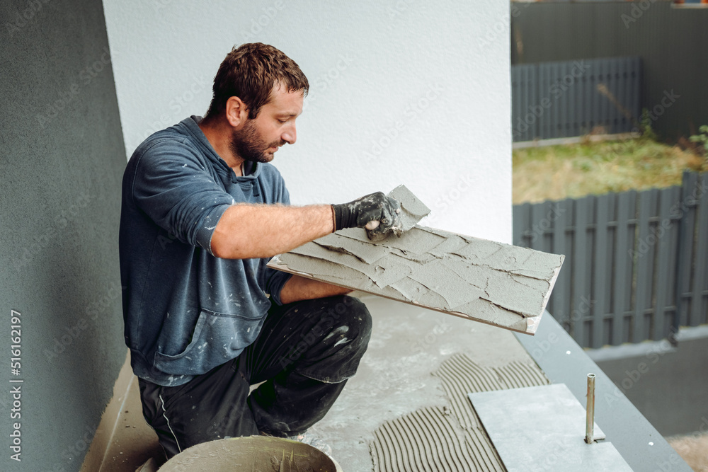 Wall Mural Professional construction worker, tiler laying adhesive and placing ceramic tiles on balcony floor