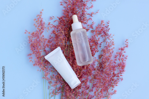 Cosmetic bottles with pink flower grass  (Natal grass,Natal redtop,Melinis repens) on blue background photo