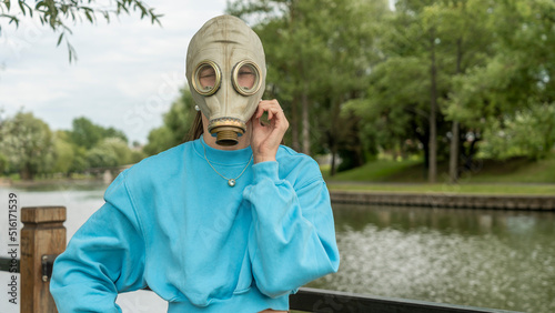 Girl with long hair in a gas mask on the river bank. Alienation in the city. Fashion, ecology and loneliness concepts.
