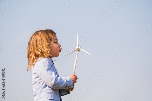 Closeup of little boy blowing a wind turbine toy and studying how green energy works from a young age - Concept of future generation and enewable Energy