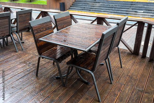 Empty wet wooden table and chairs in a street cafeteria during the rain. Street city life in the rain © LariBat