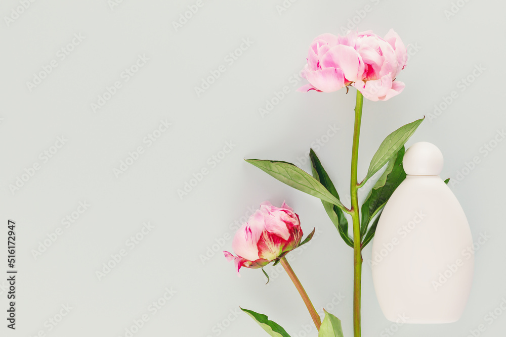Mock up of natural, flower beauty product. White cosmetic bottle with two beautiful, pink peonies on a blue background with copy space. Minimalistic composition with flowers and cosmetic product