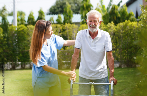A young nurse walks with an old man in the park. Happy active old man trying to walk with the help of a female doctor