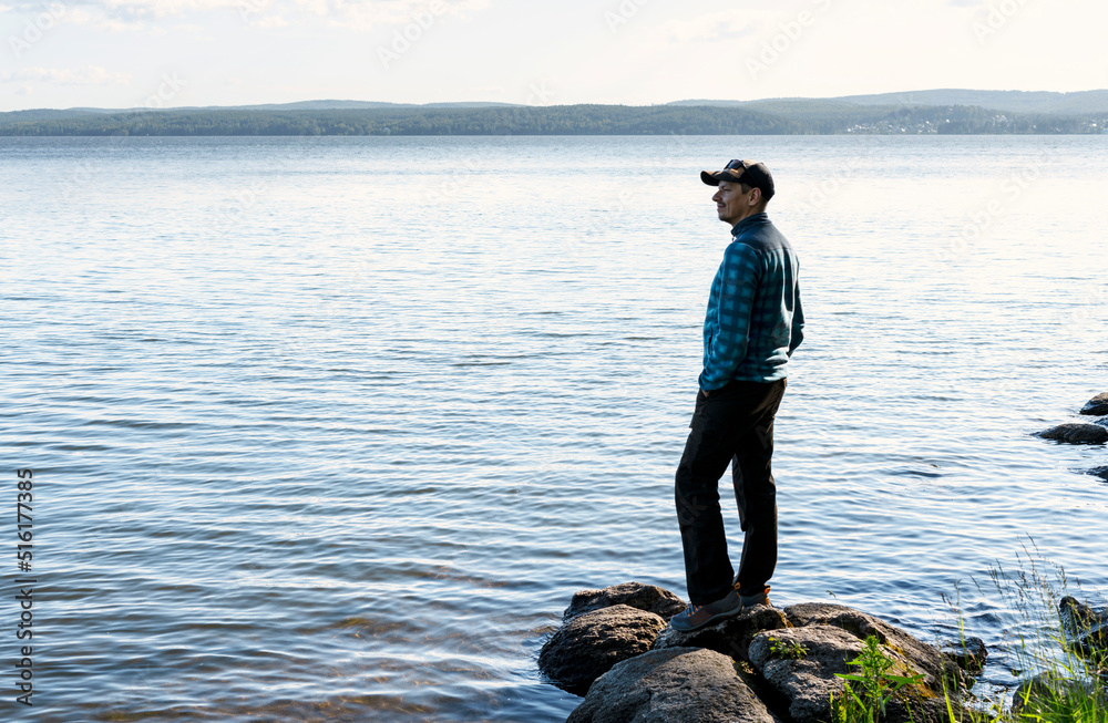 young man in a cap looking at the view of the lake or river standing on the stones Enjoying nature landscape