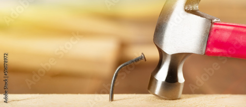 A bent nail in a wooden board with a hammer in the background