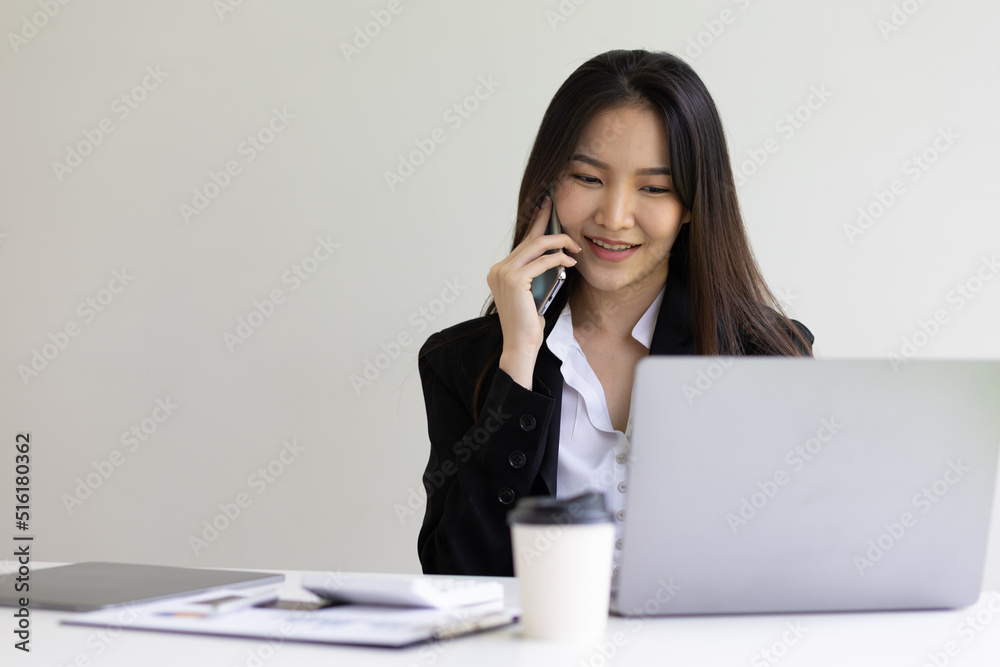 Asian businesswoman talking on mobile phone working on laptop in office. Happy business woman talking on mobile phone while analyzing weekly schedule in laptop. Asian businesswoman talking on mobile phone working on laptop in office. Happy business woman talking on mobile phone while analyzing weekly schedule in laptop.