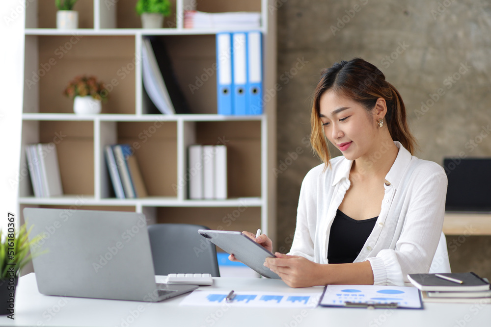 Attractive young Asian businesswoman in the office holding a tablet working on documents at her desk. Attractive young Asian businesswoman in the office holding a tablet working on documents at her desk.