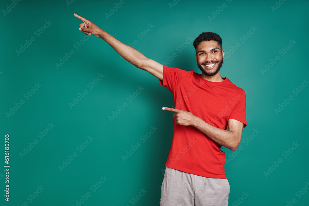 Cheerful African man pointing away while standing against green background