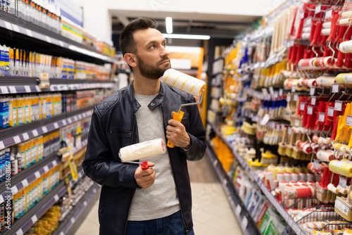Foto a man in a hardware store chooses brushes and rollers for painting work