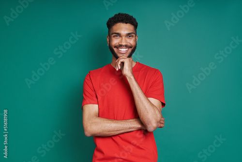 Happy African man holding hand on chin and smiling while standing against green background