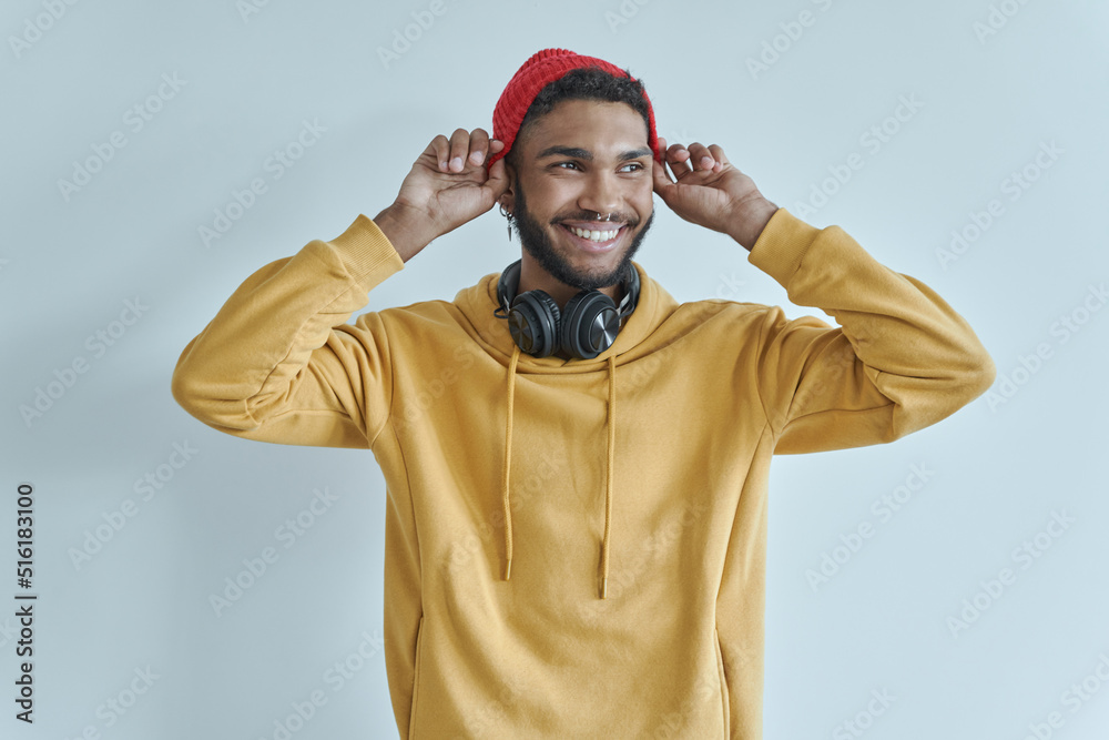 Handsome African man adjusting his hat and smiling while standing against the wall Handsome African man adjusting his hat and smiling while standing against the wall