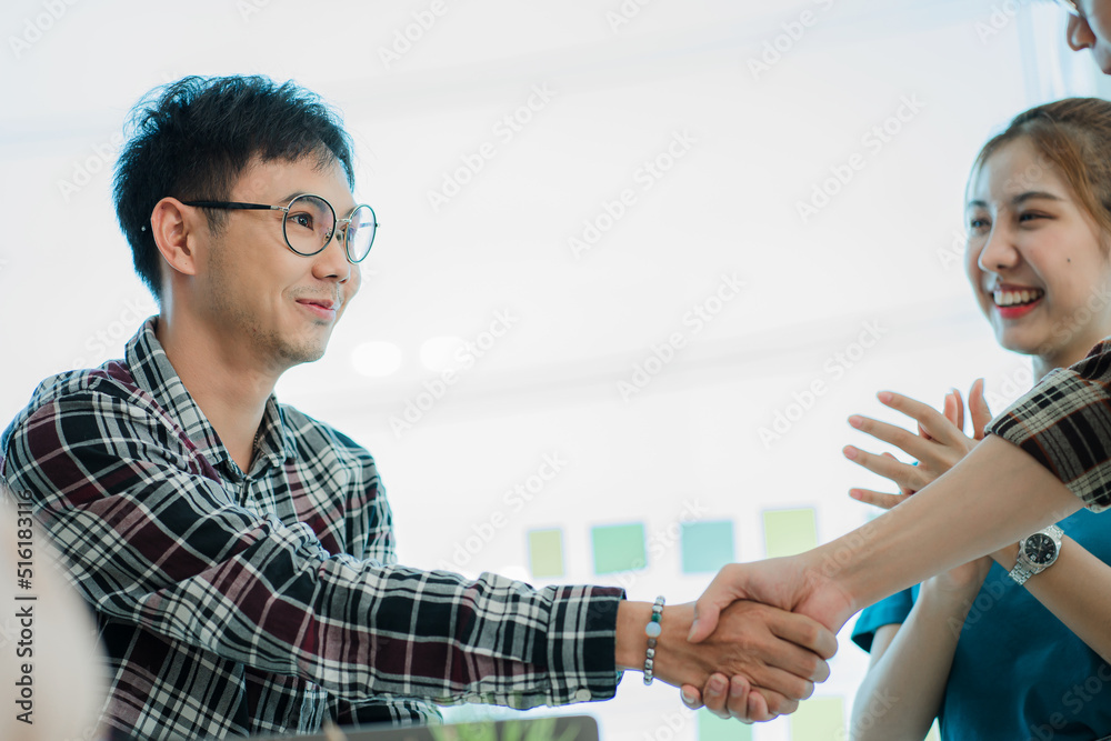 young business people shaking hands Two handsome young men shake hands with smiles at the office with a colleague with a graph in the background. young business people shaking hands Two handsome young men shake hands with smiles at the office with a colleague with a graph in the background.