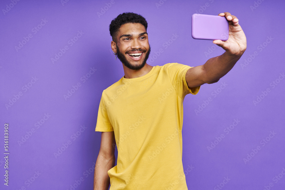 Happy African man making selfie by smart phone while standing against purple background Happy African man making selfie by smart phone while standing against purple background