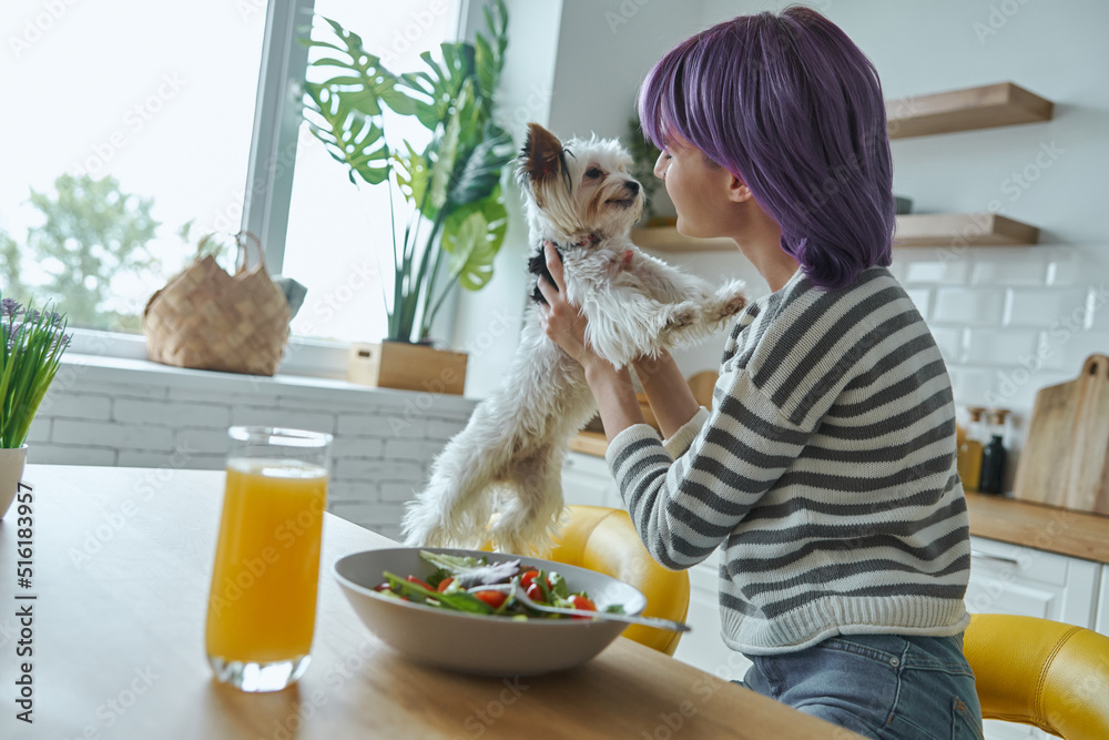 Young woman spending time with her cute little dog while sitting at the kitchen island