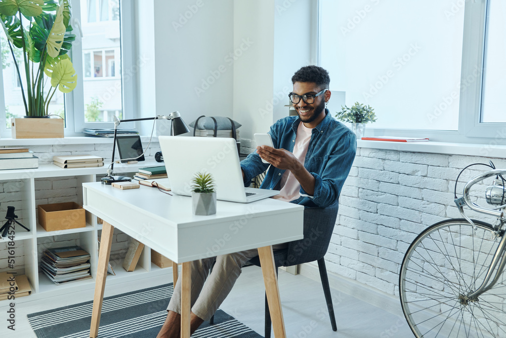 Cheerful young African man using smart phone while working in office Cheerful young African man using smart phone while working in office