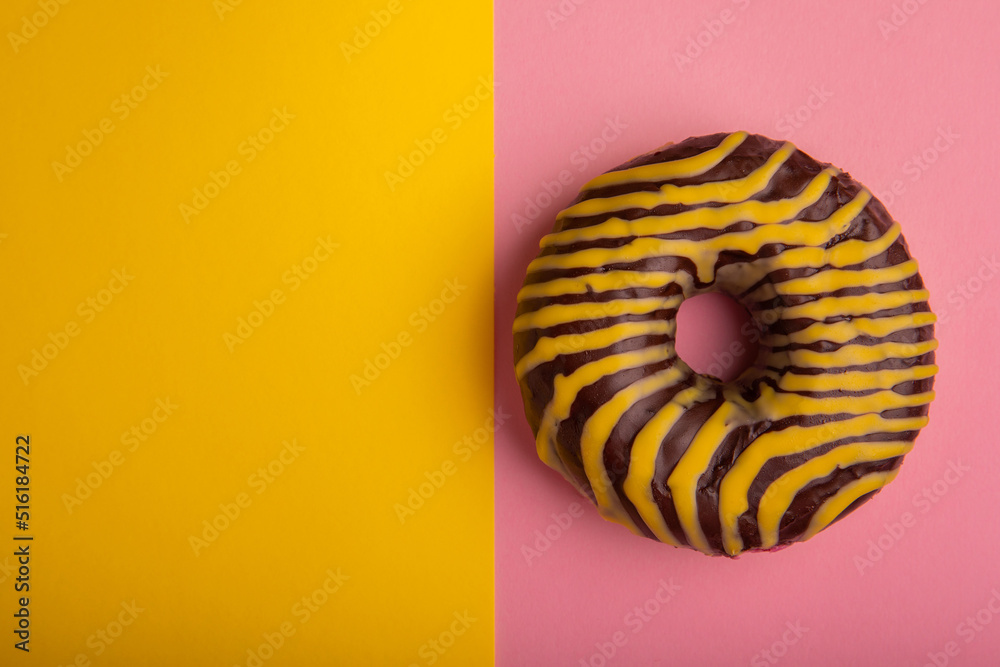 Donut on a pink-yellow background. Chocolate donut with yellow icing on