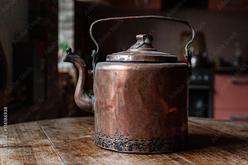 an old copper kettle stands in the kitchen on a wooden table an old copper kettle stands in the kitchen on a wooden table