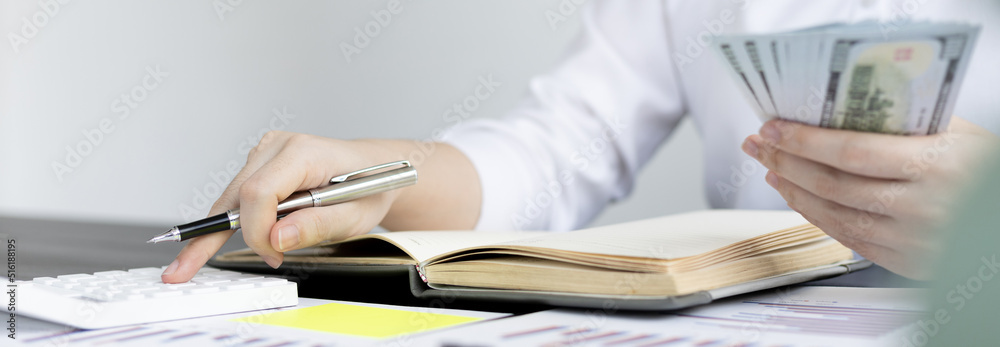 Business women press calculator to calculate company income and expenses, Calculating financial and tax information, Hand holding dollar bills, Financial savings and income tax calculation concept. Business women press calculator to calculate company income and expenses, Calculating financial and tax information, Hand holding dollar bills, Financial savings and income tax calculation concept.