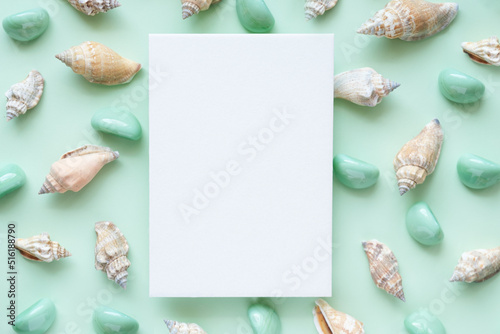 Obraz na plátně White blank vertical paper card against sea shells and smooth stones on a pale green background