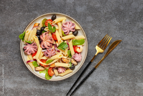 Penne pasta with vegetables and seafood in a plate on the table. Top View