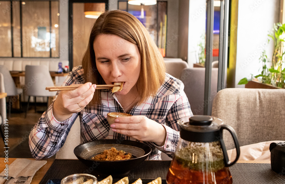 a girl eats japanese food with chopsticks in a restaurant. teapot with tea on the table a girl eats japanese food with chopsticks in a restaurant. teapot with tea on the table