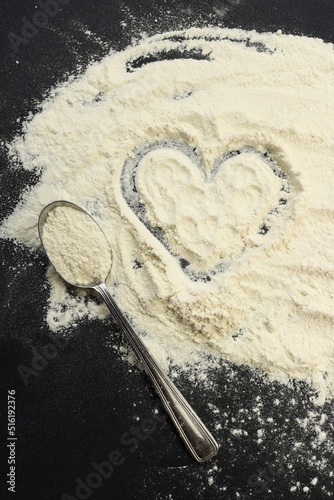 Heart on flour on black background.Spoon with flour